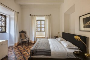 Classic hotel room with a bed, chair, and lamp, set against a geometric-patterned floor.