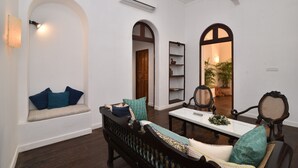 A living room with a sofa, chairs, a table, and a bookshelf. - Mateus Boutique Hotel (Panaji)