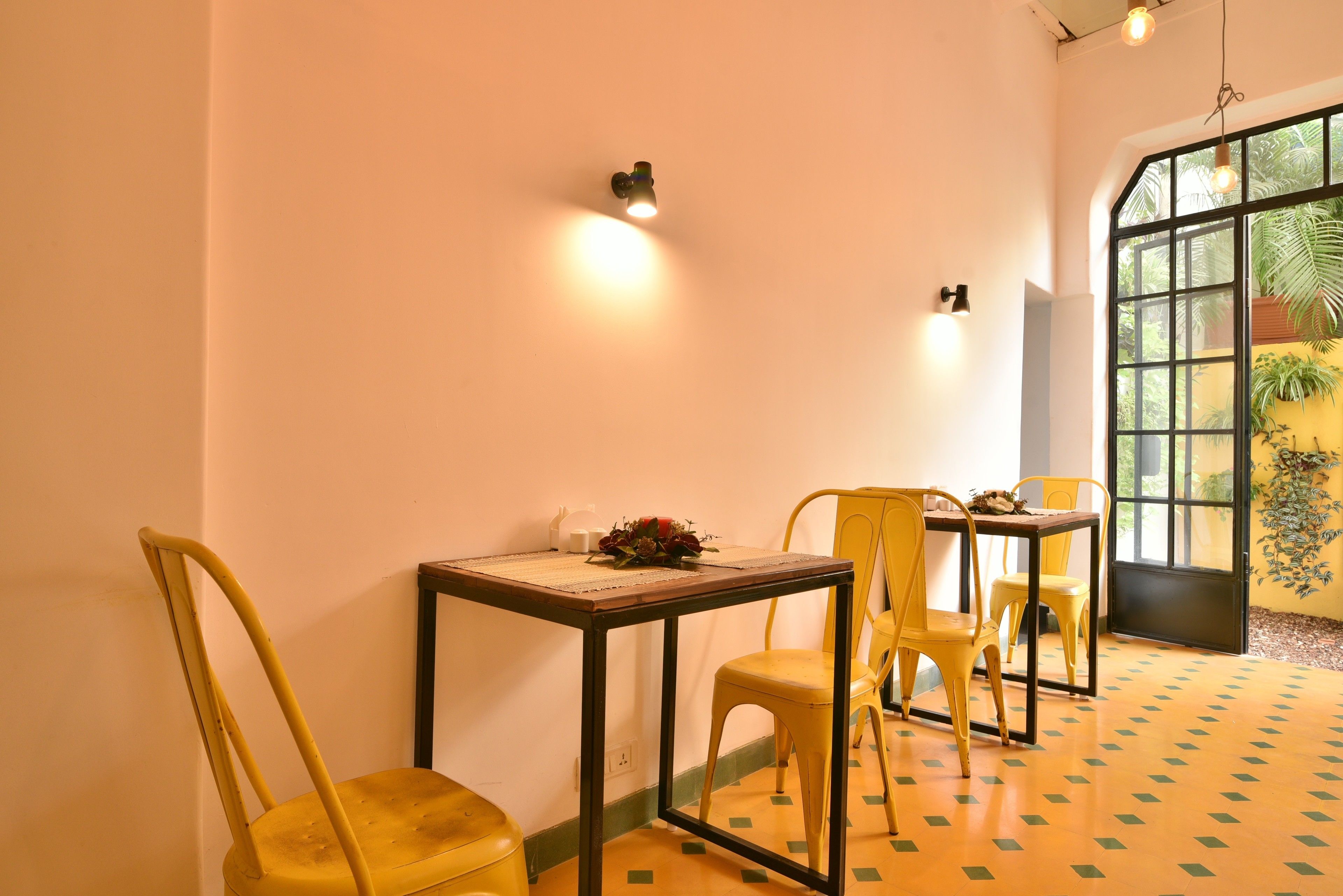 A dining area with yellow chairs and a table, a wall-mounted light, and a window with a view of greenery.