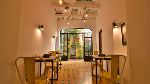 A dining area with yellow chairs and tables, a patterned floor, and a view of the outside through a large window. - Mateus Boutique Hotel (Panaji)
