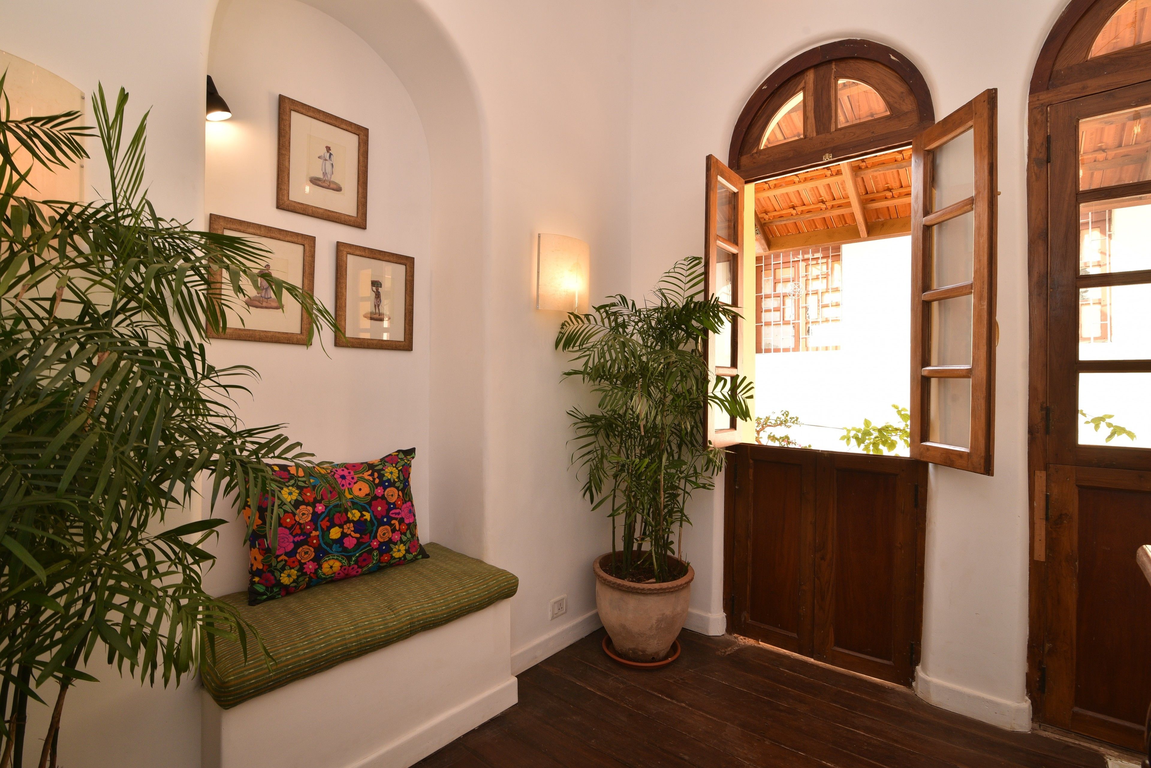 A hallway with a wooden bench, a potted plant, framed pictures on the wall, and an open wooden door leading to another room.