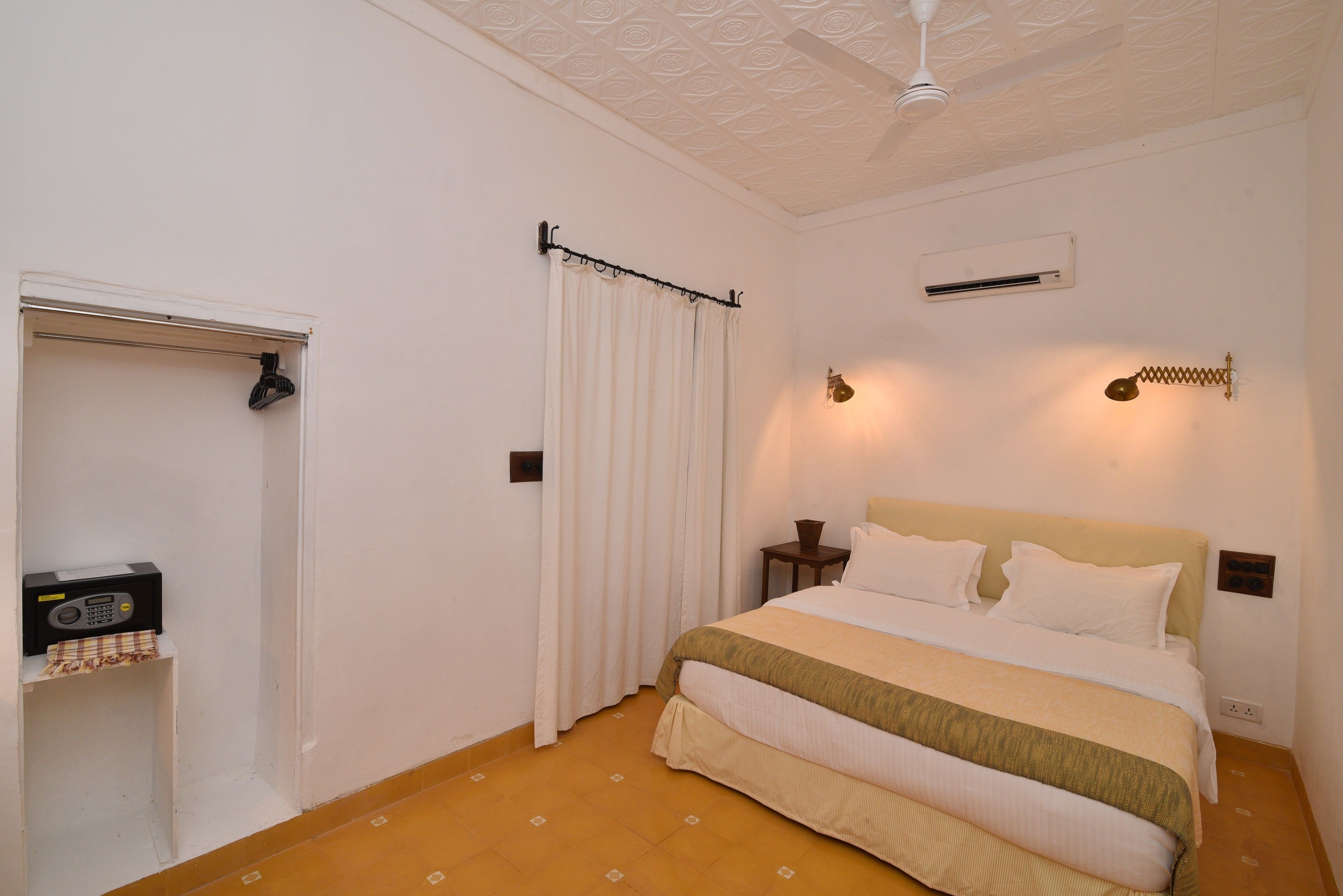 A hotel room with a bed, a radio, a curtain, a ceiling fan, and wall-mounted lights.