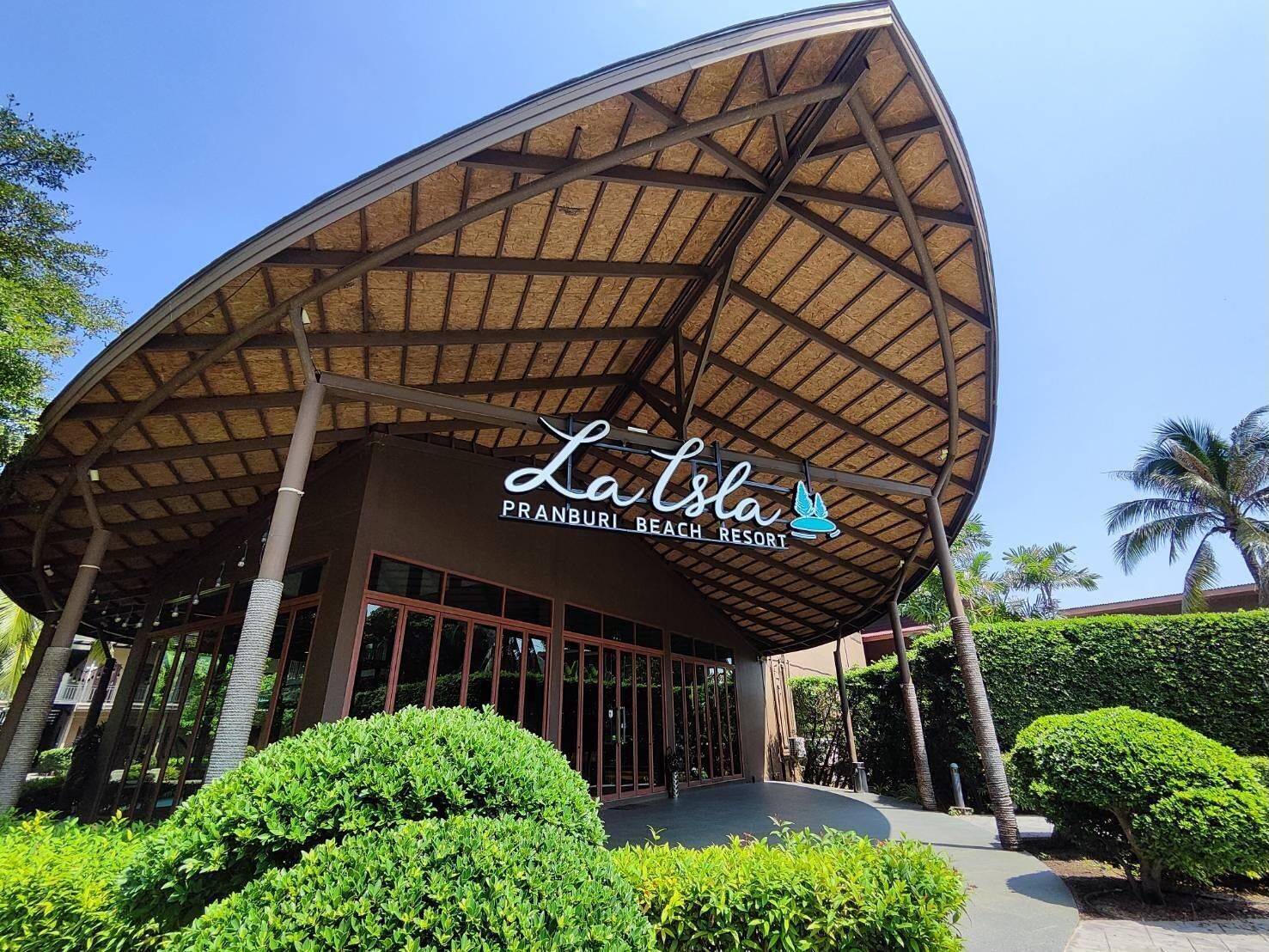 A modern building with a curved roof and a sign that reads "La Isla PRANBURI BEACH RESORT".