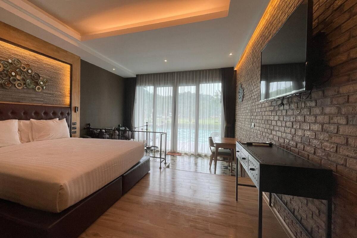 Een moderne hotelkamer met een groot bed, een bureau, een televisie en een balkon met uitzicht op het zwembad.
