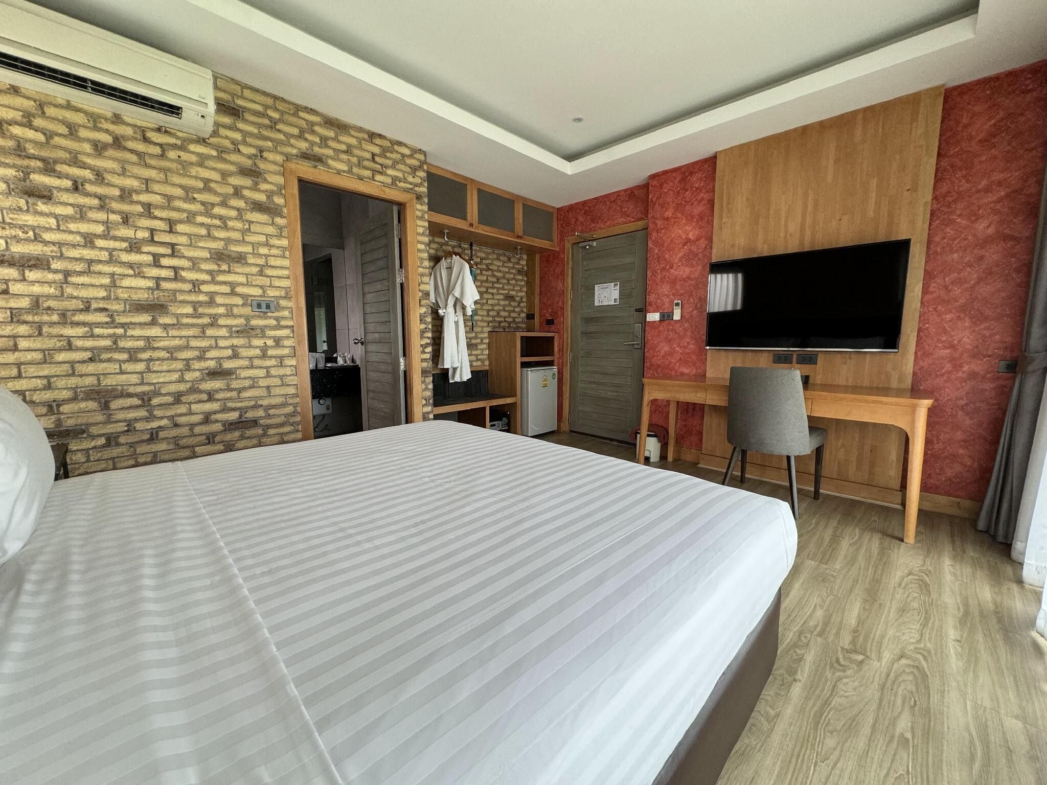 A hotel room with a large bed, a desk with a chair, a TV, and a wardrobe.