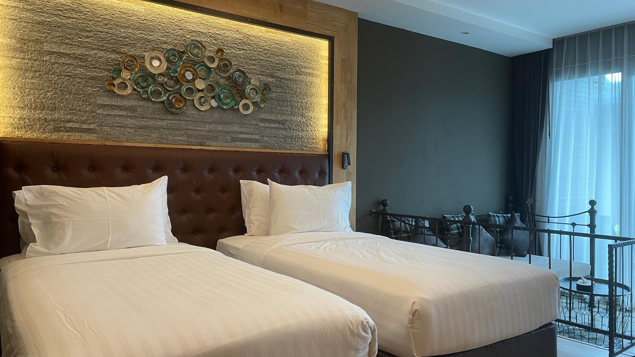 A hotel room with two beds, a decorative wall, a balcony with a railing, and a view of the outdoors.