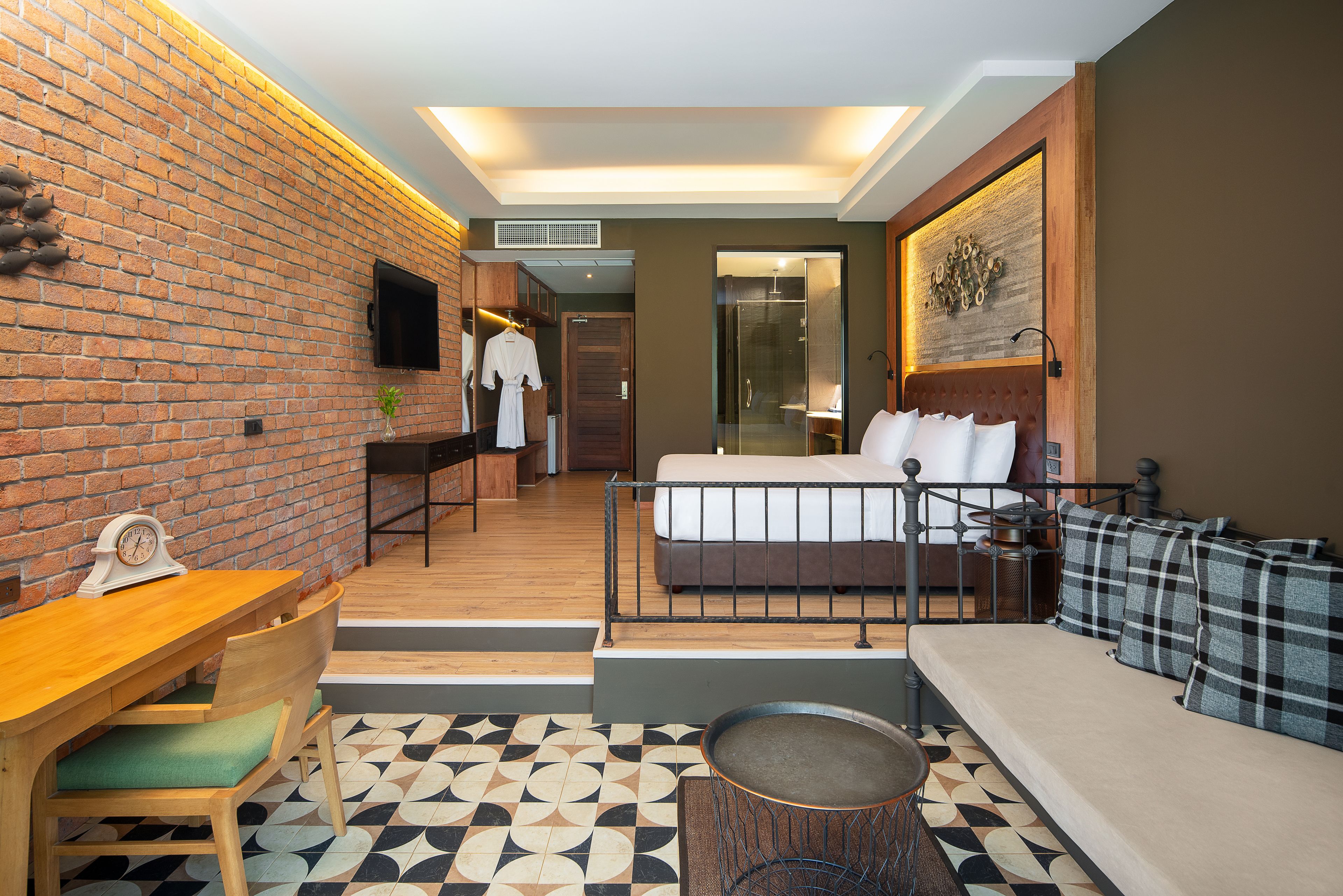 Habitación de hotel con pared de ladrillo, una cama con cabecero, un sofá, una mesa de comedor y un televisor.