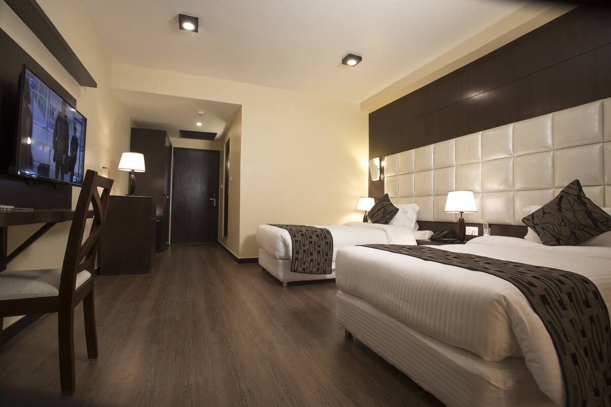 A hotel room with a large bed, a smaller bed, a desk with a chair, a television, and a lamp.