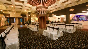 Un salón de banquetes con filas de sillas blancas, una columna decorativa en el centro y una alfombra estampada.