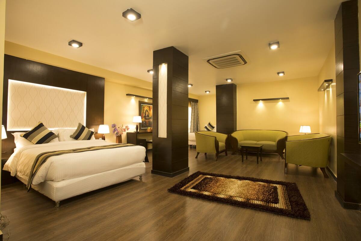 A modern hotel room with a large bed, a sitting area with a sofa and chairs, and a small table.