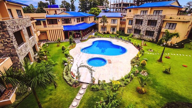A hotel with a central swimming pool surrounded by well-maintained lawns and a few palm trees.