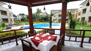 A dining area with a table set for four, overlooking a swimming pool and a landscaped garden.