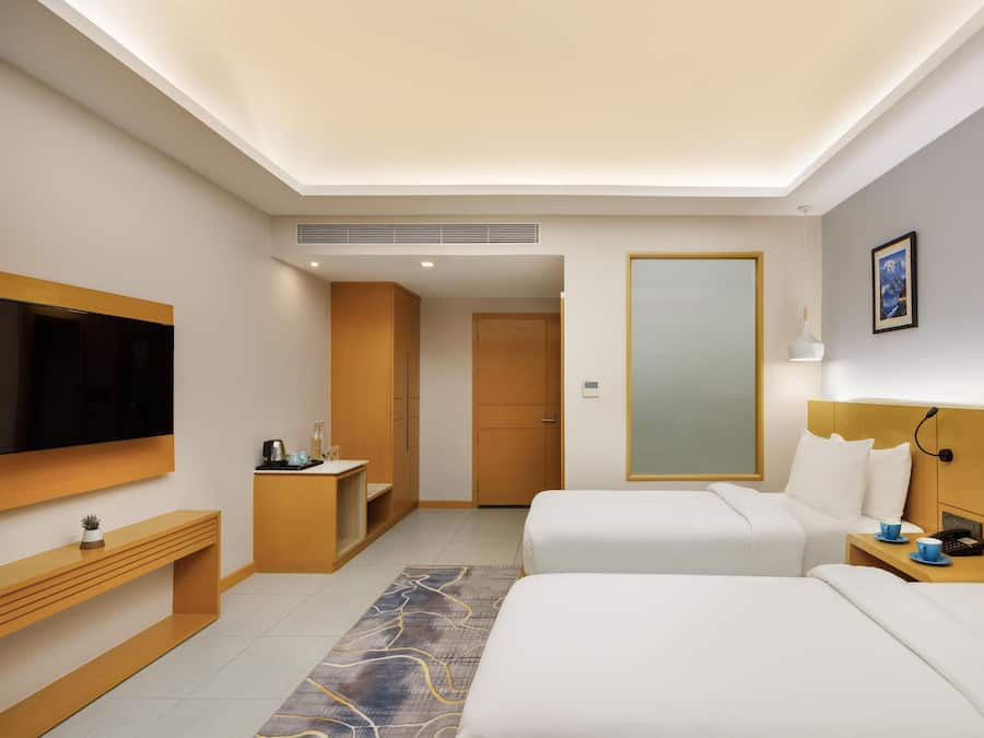 Habitación de hotel con cama, mesita de noche, televisión y un amplio ventanal.