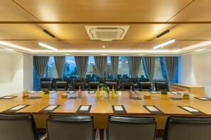 A conference room with a long table, multiple chairs, and a view of trees through large windows. - Best Western Siraichuli Hotel (Bharatpur)