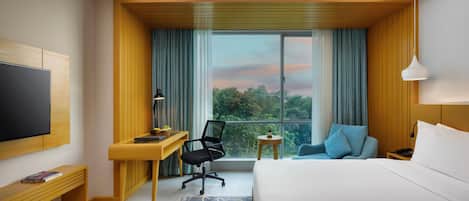 Habitación de hotel con cama, escritorio, silla, televisor y vista al exterior.