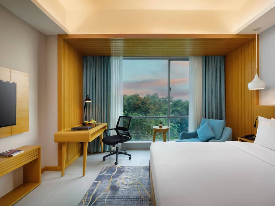 A hotel room with a bed, a desk, a chair, a TV, and a view of the outdoors.