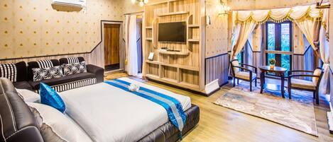 A spacious bedroom with a large bed, a sofa, a TV, and a seating area with curtains.