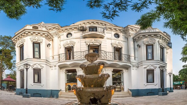 Een historisch gebouw met versierde architectuur, een centrale fontein en een bord waarop staat 'Royal Estate'.