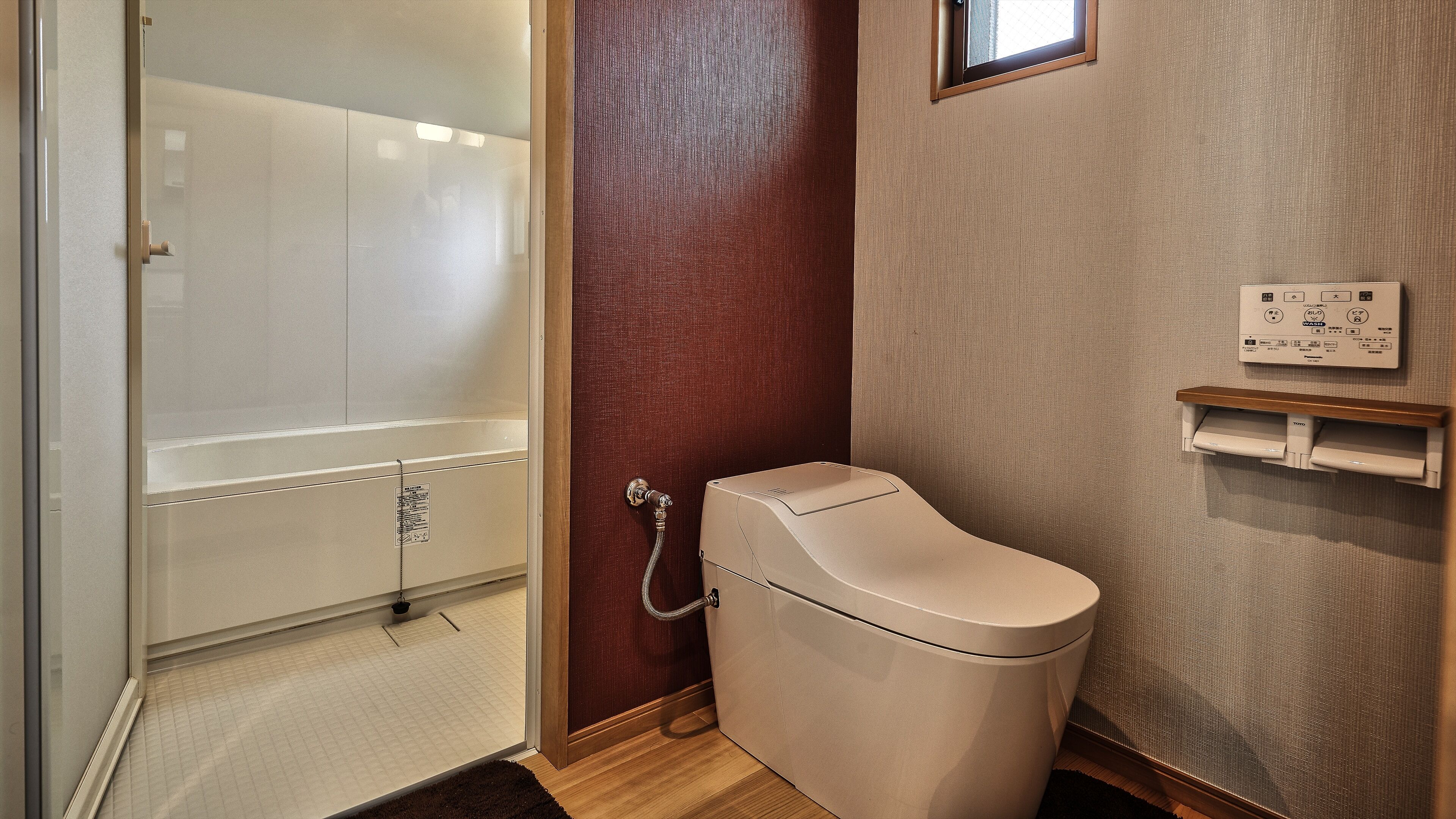 A compact bathroom with a glass shower enclosure, a toilet, and a towel dispenser.