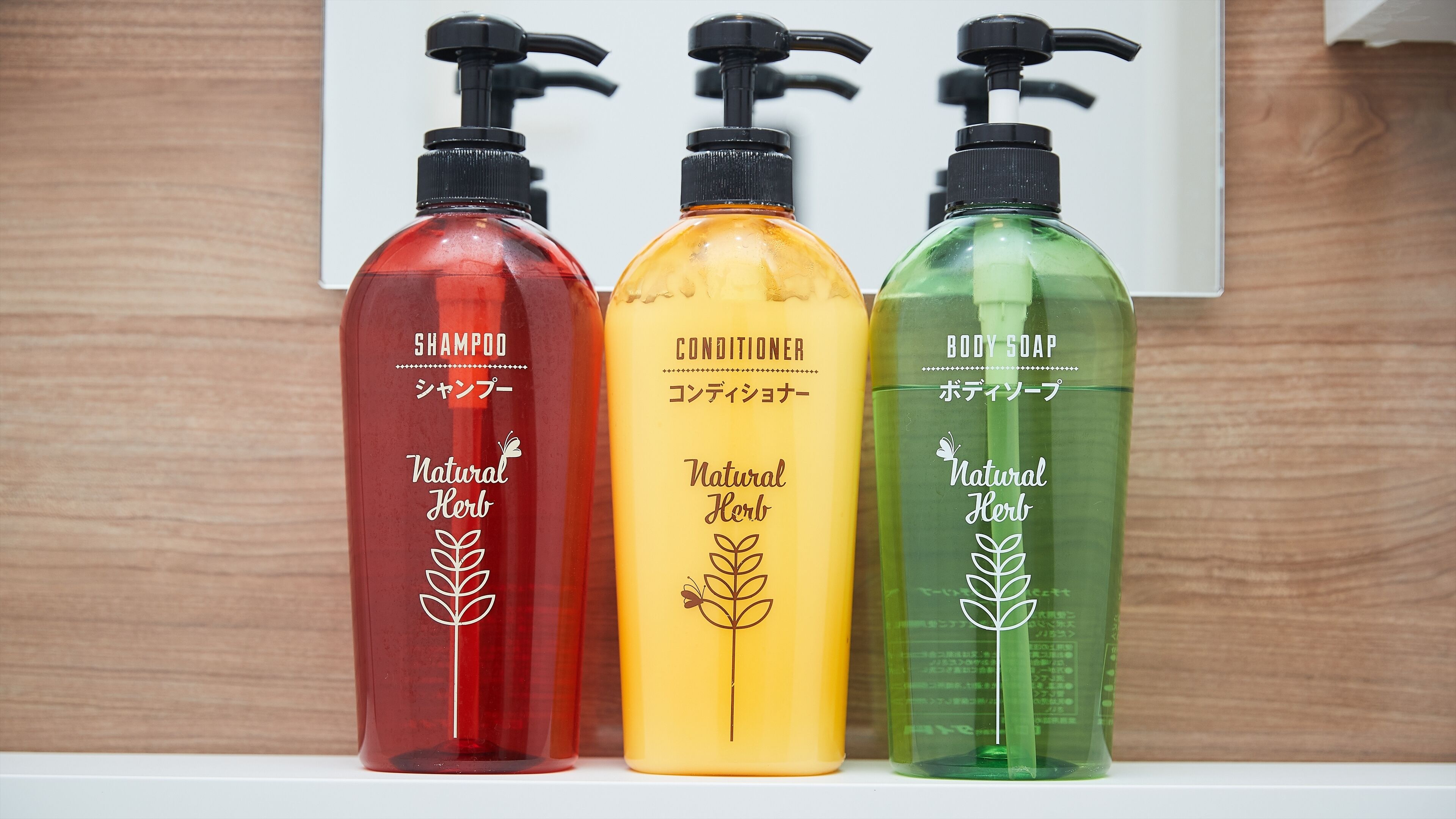 Three bottles of natural herb shampoo, conditioner, and body soap on a shelf.