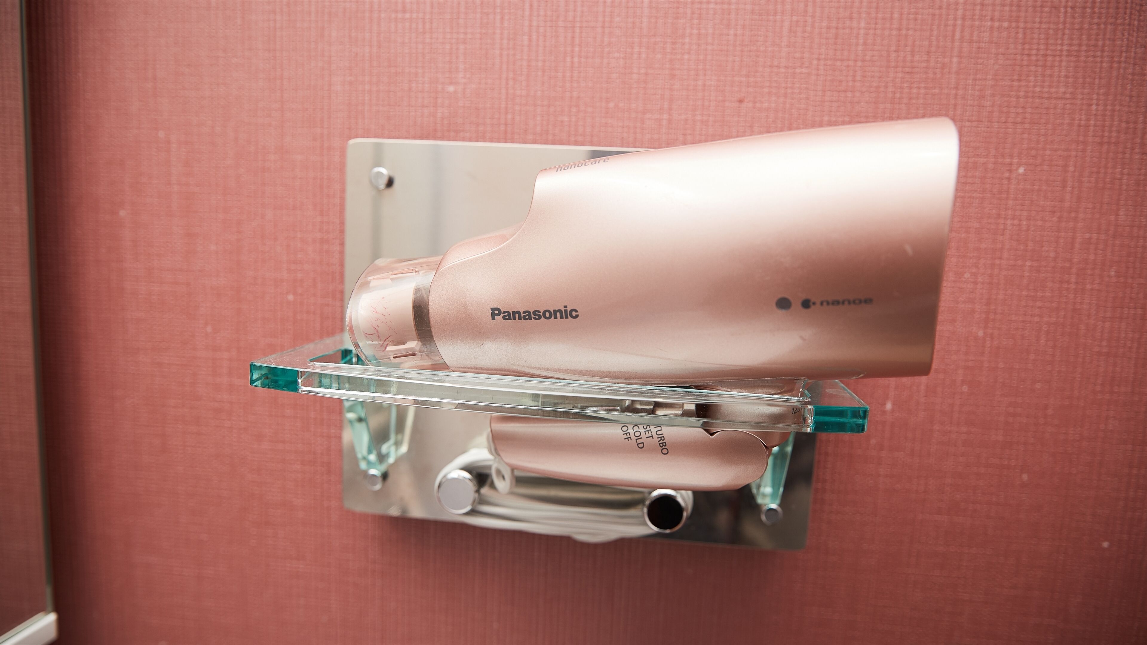 A Panasonic hairdryer mounted on a wall with a clear glass stand.