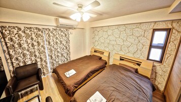 Habitación pequeña con dos camas individuales, un escritorio, una silla y un ventilador de techo.