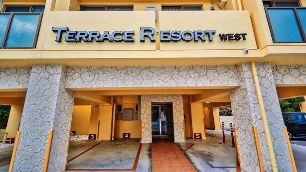 La entrada del Terrace Resort West, con espacios de estacionamiento numerados y fachada de piedra.