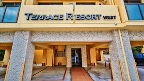 The entrance of Terrace Resort West with numbered parking bays and a stone facade. - Terrace Resort Chatan West (Chatan)
