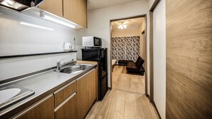 Cocina compacta con lavabo, microondas y hervidor, que da paso a una sala de estar con sofá y cortinas estampadas.