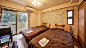Habitación de hotel con dos camas, un balcón, una silla y un escritorio con vistas.