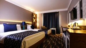 A hotel room with two beds, a desk, a chair, a TV, and a window with curtains. - Sivas Buyuk Hotel (Sivas)