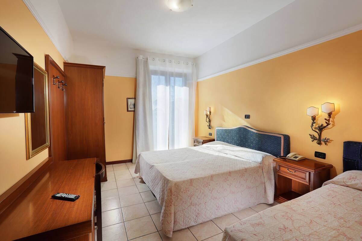 A hotel room with two beds, a desk, a television, a nightstand, and a window with curtains.