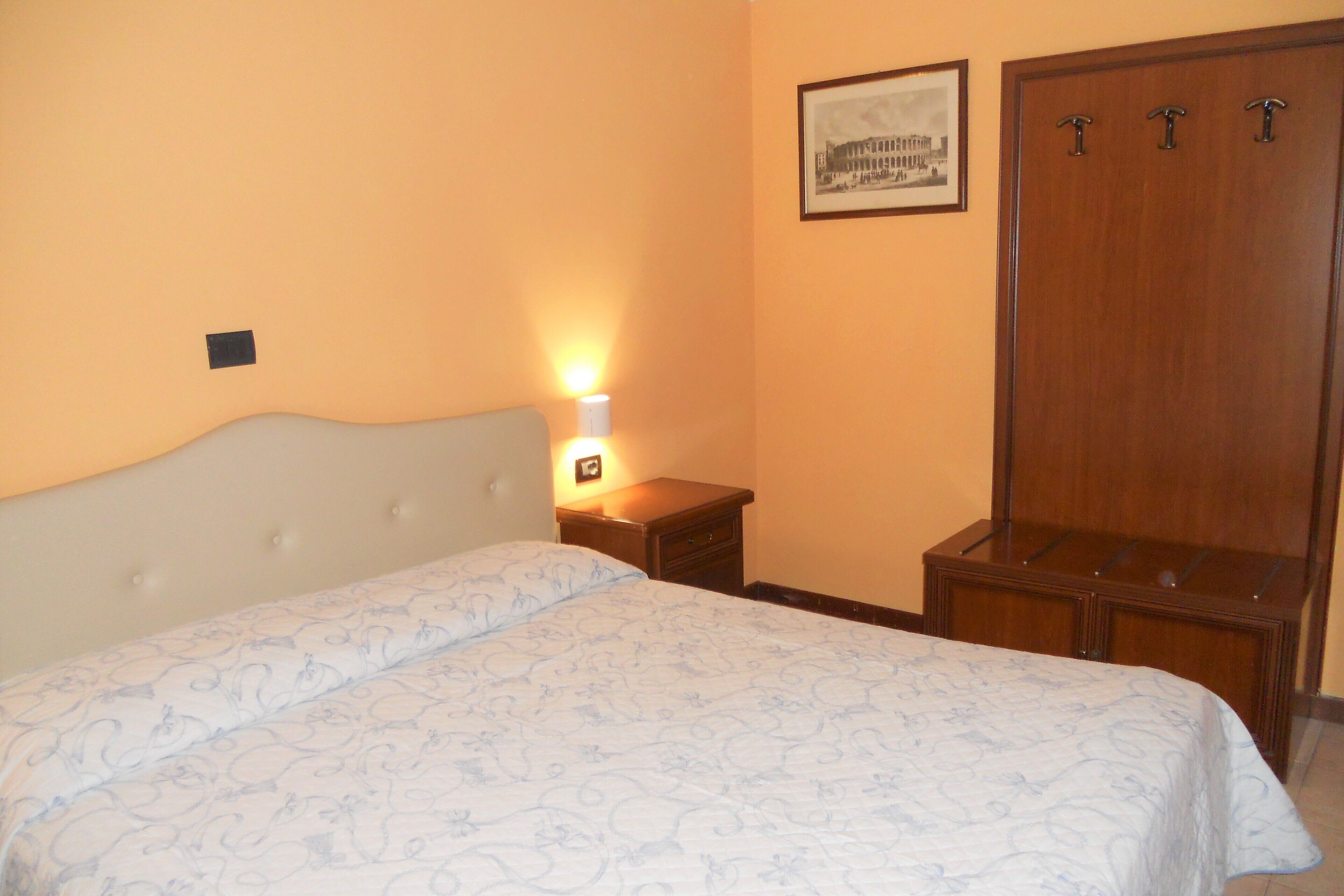 Un dormitorio con cama, mesita de noche, cómoda y un cuadro en la pared.