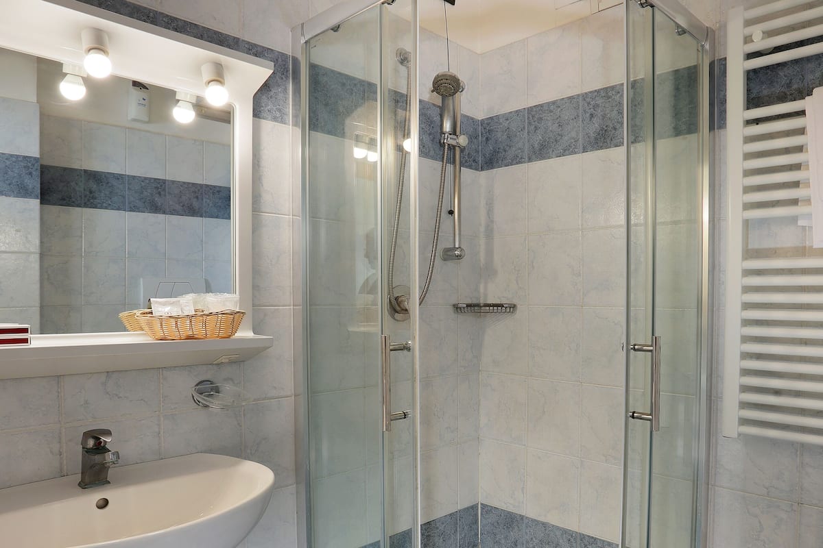 A bathroom with a glass-enclosed shower, a pedestal sink, and a mirror with lights.