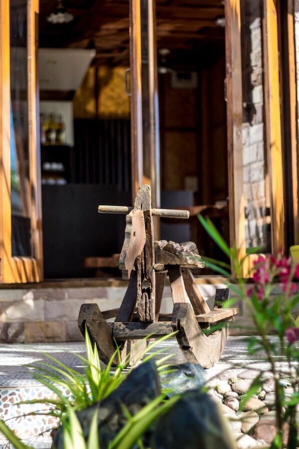 A rustic outdoor setting with a wooden structure, possibly a rustic bench or seating area, surrounded by greenery and rocks.
