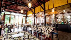 Ein Restaurant mit hohen Decken, großen Fenstern und Tischen mit gemusterten Tischdecken.