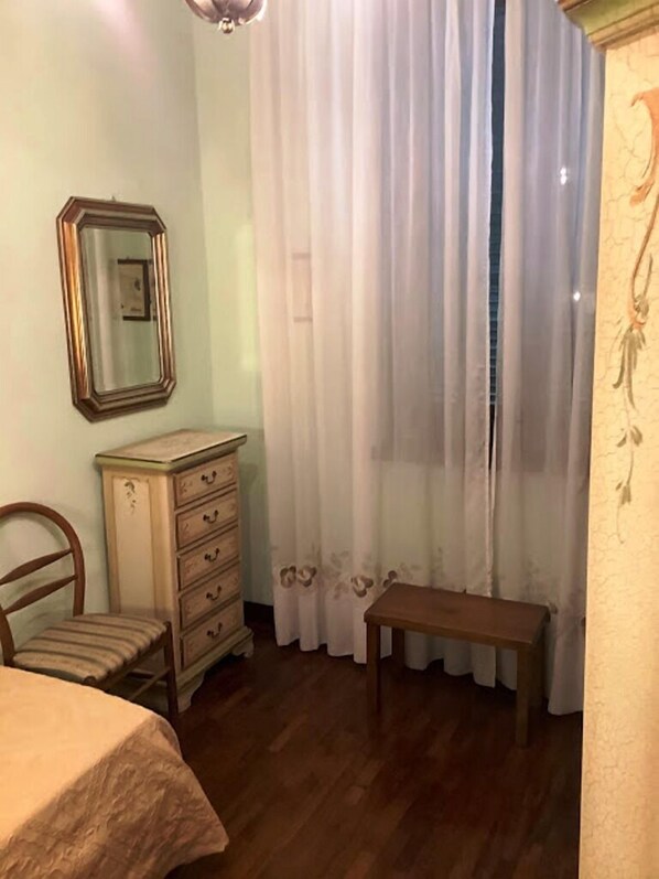 A bedroom with a bed, a wooden dresser, a chair, a bench, and a window with white curtains.