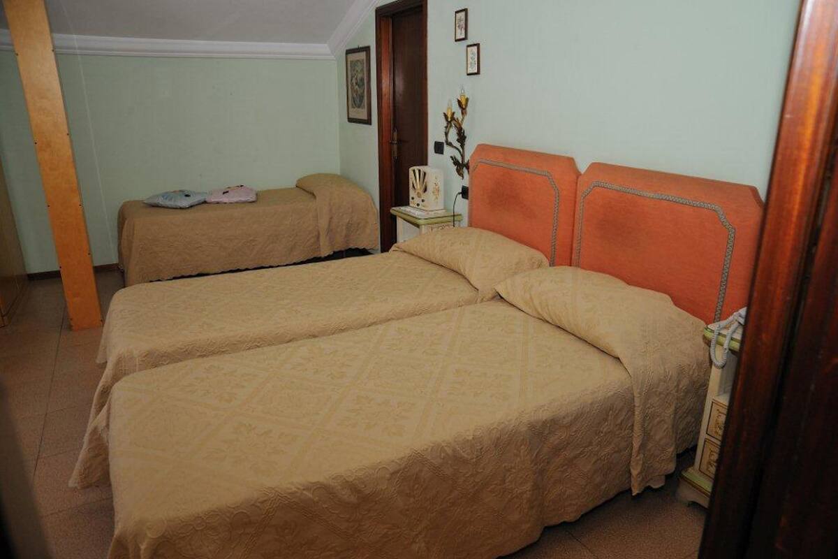A room with two beds, each with a beige bedspread, a wooden headboard, and a small bedside table with a lamp.