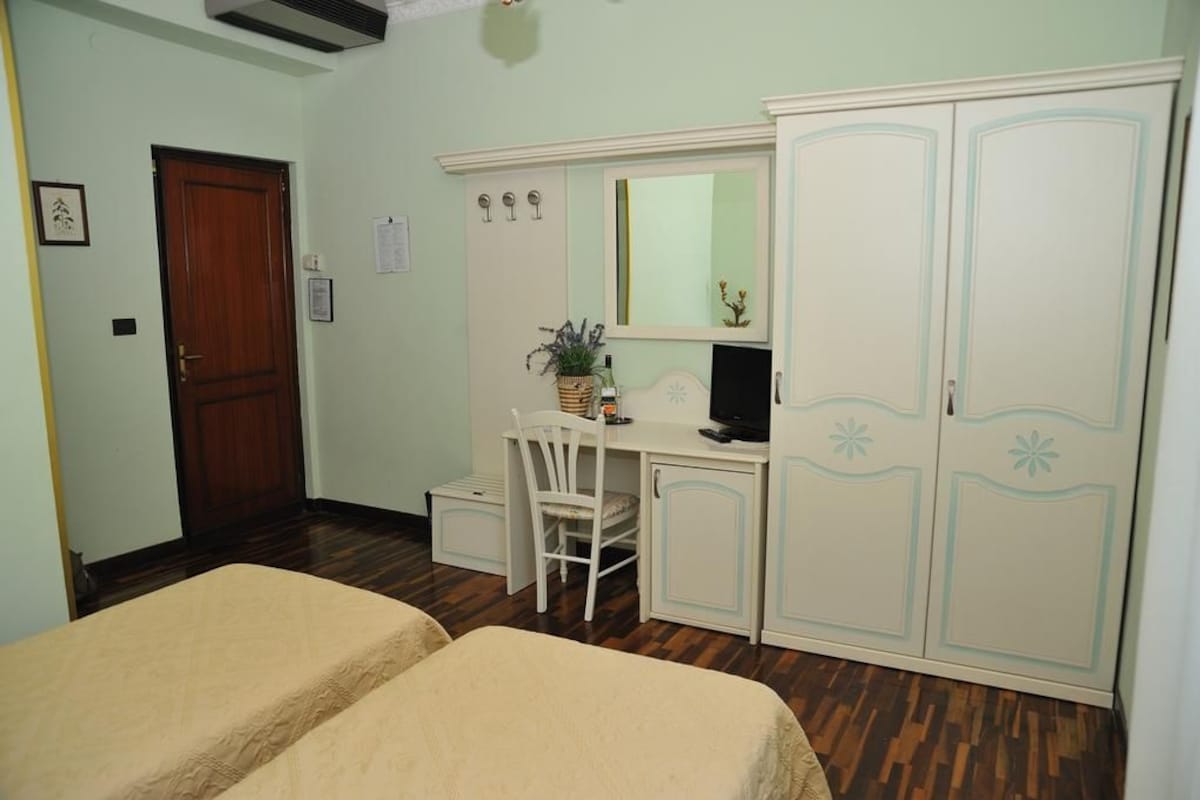 A bedroom with two beds, a desk with a chair, a wardrobe, and a door.