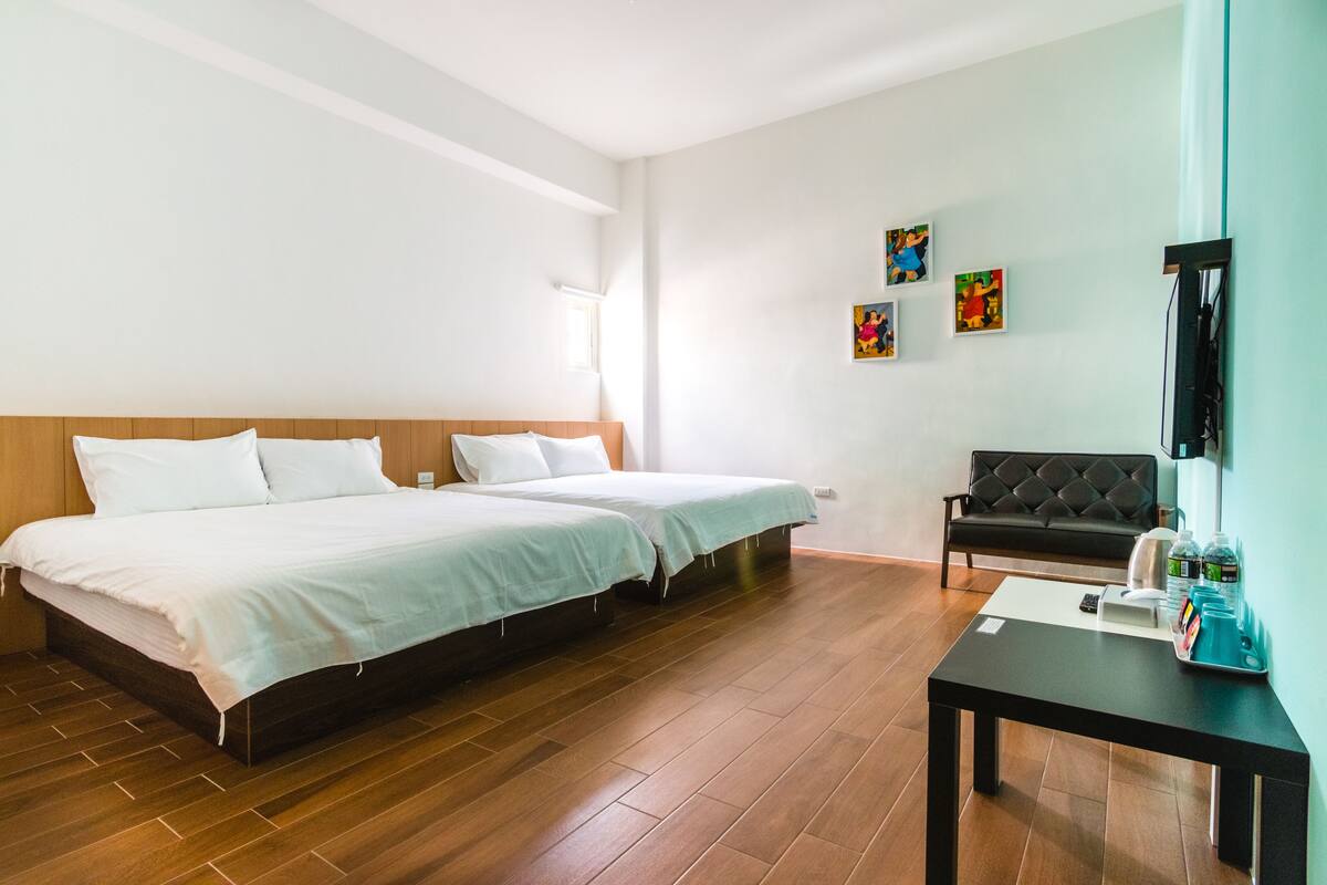 A hotel room with two beds, a sofa, a table with toiletries, and artwork on the wall.