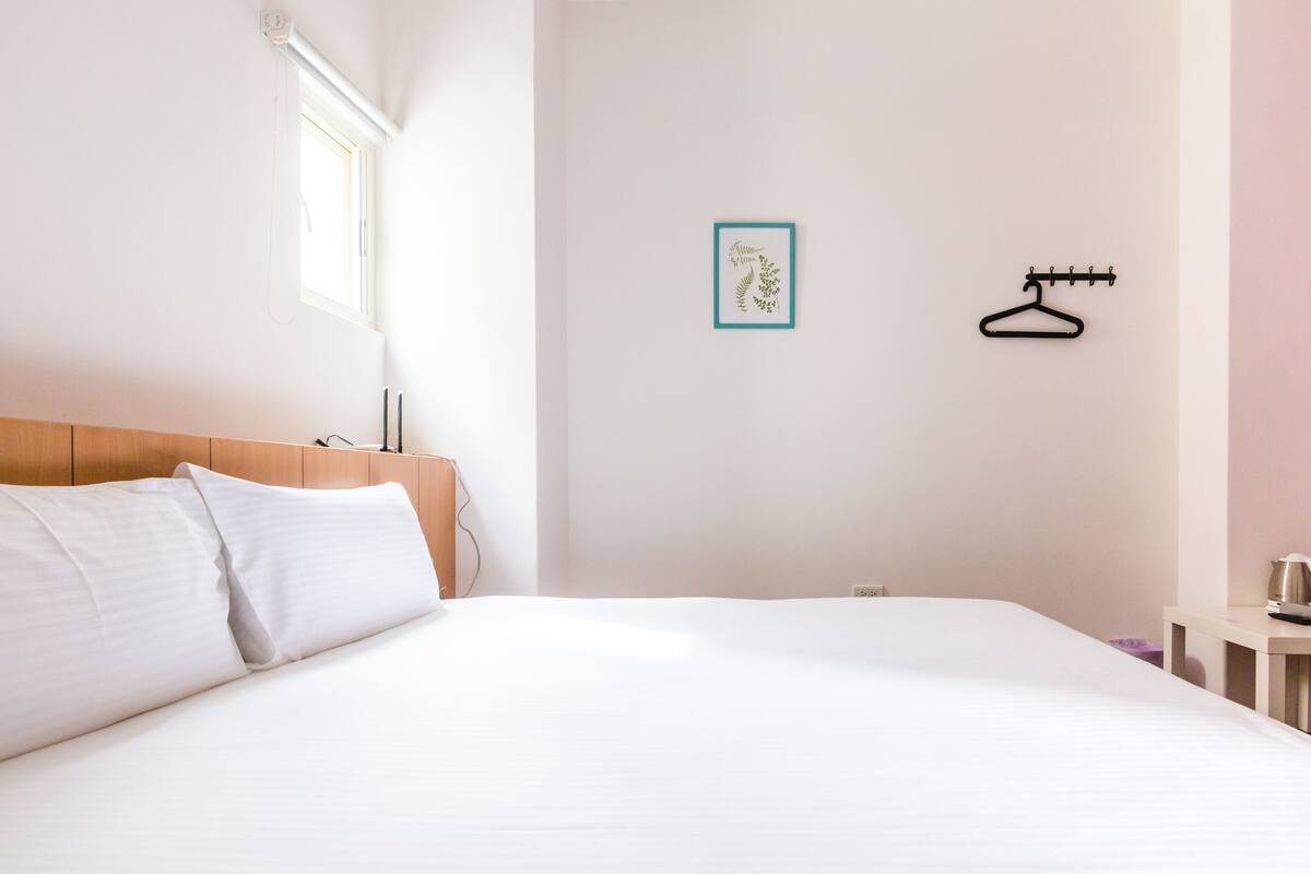 A neatly made bed with white linens in a room with a wooden headboard.