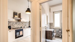 Una cocina moderna con armarios blancos, un salpicadero decorado y una lámpara colgante negra.