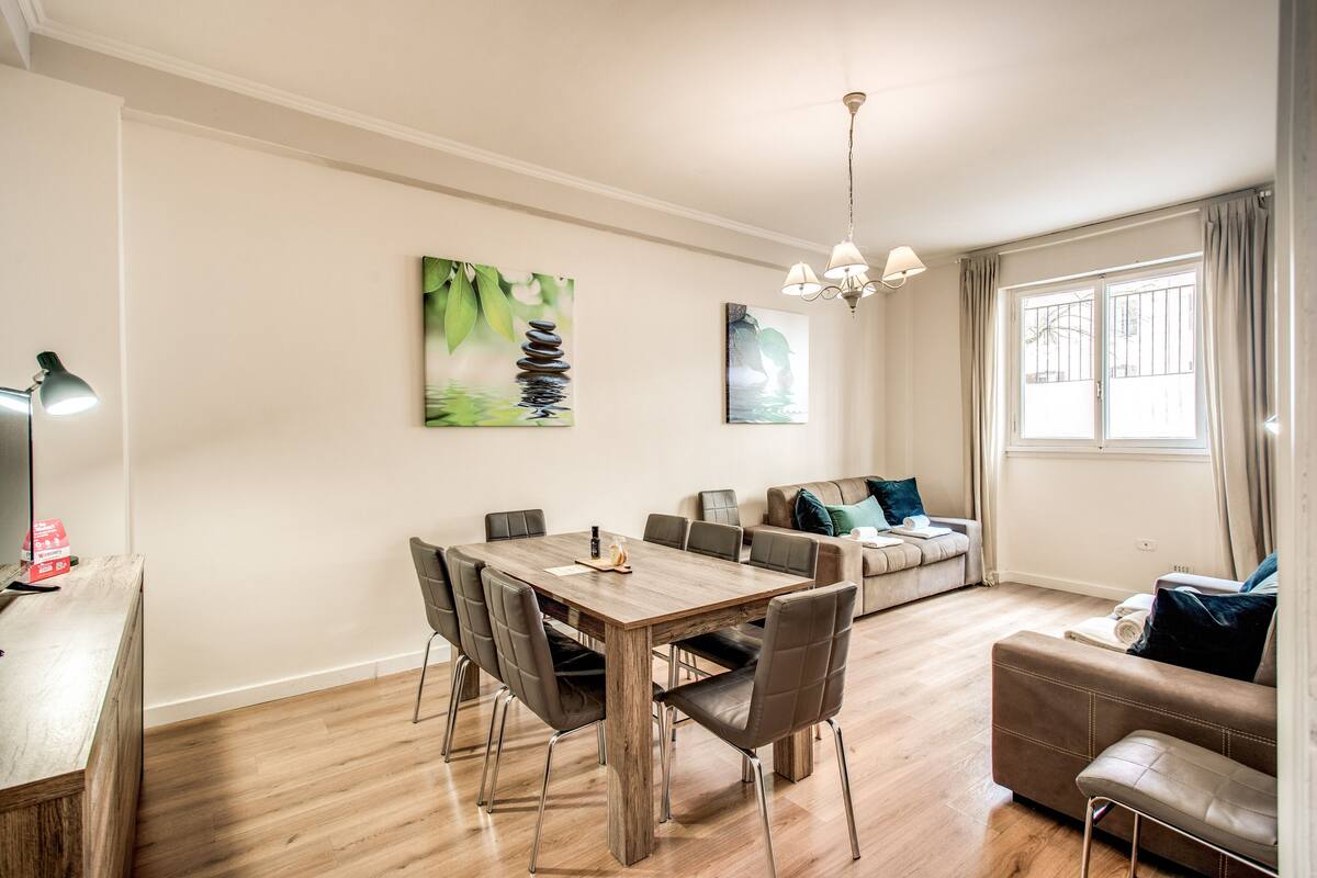 Uma sala de estar moderna com uma mesa de jantar de madeira, sofás de couro e uma grande janela com cortinas.