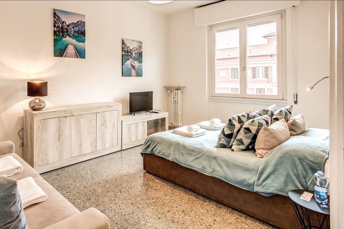 Um quarto com cama, sofá, televisão e obras de arte nas paredes.