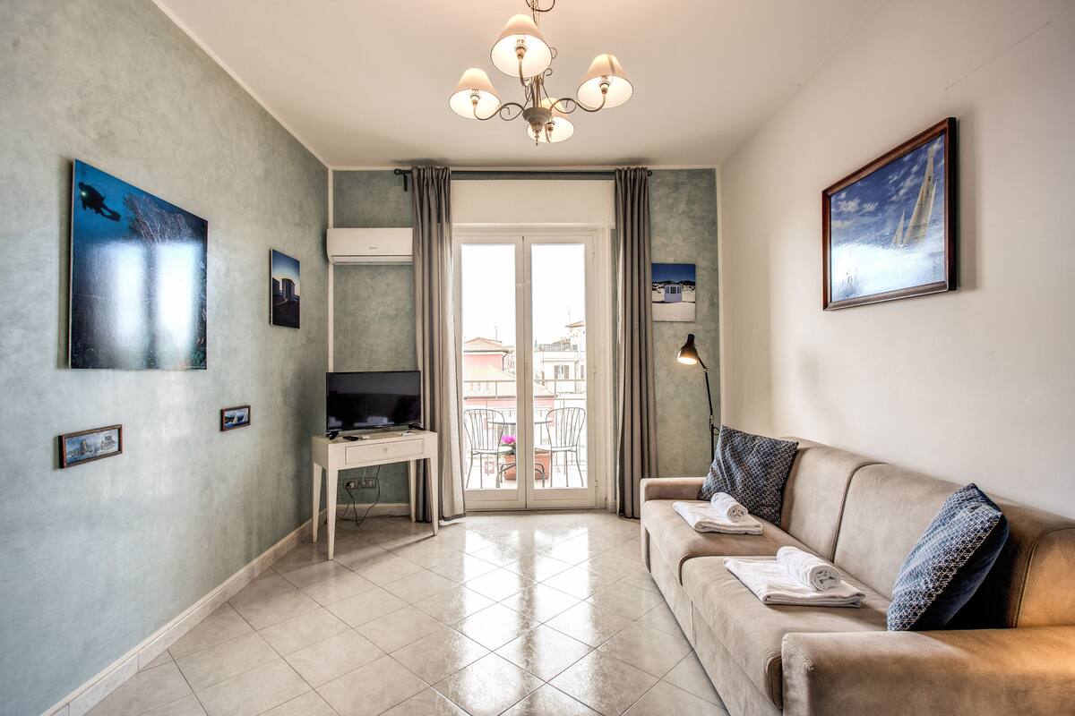 Uma sala de estar com sofá, televisão, escrivaninha e varanda com vista.