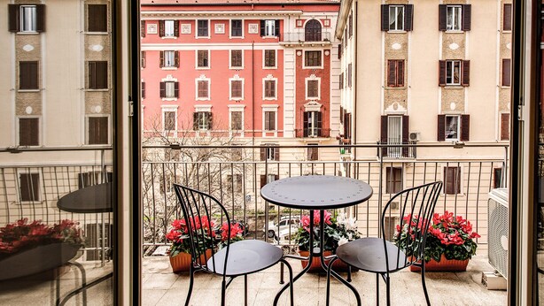 Un balcón con dos sillas y una mesa, con vistas a una hilera de edificios con balcones.
