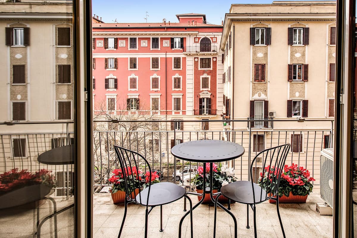 Varanda com duas cadeiras e uma mesa, com vista para uma fileira de edifícios com varandas.