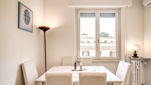 Un comedor con una mesa, sillas, una lámpara de pie y una ventana con vista a edificios.