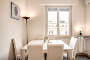 A dining area with a table, chairs, a floor lamp, and a window with a view of buildings. - Colonna Suite - San Giovanni (Rome)