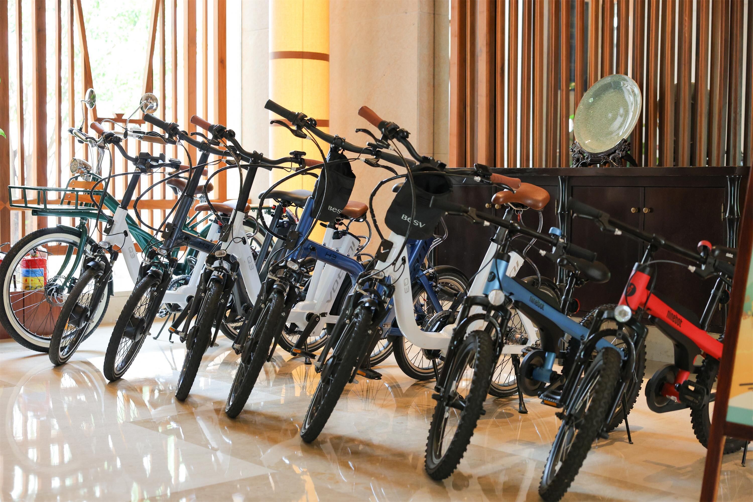 A row of bicycles parked indoors with a polished floor and wooden blinds in the background.